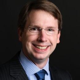 Thomas Allen - man with dark hair wearing glasses and black suit, blue gingham shirt, and navy tie